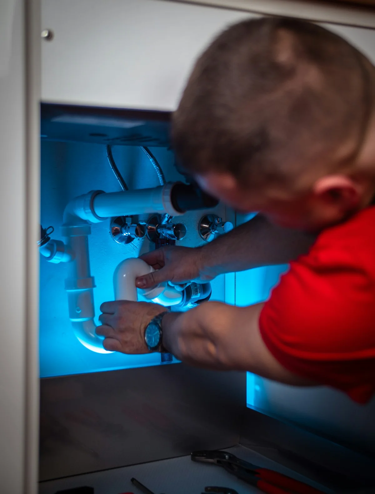 A technician working on plumbing equipment beneath a sink
